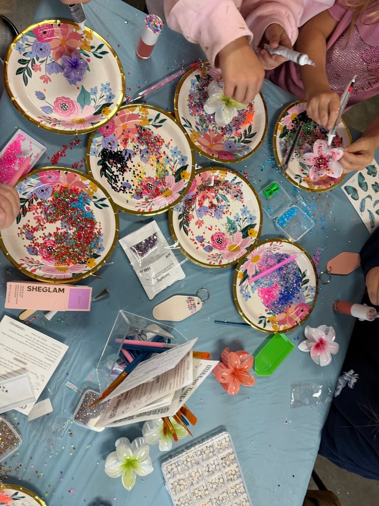 Childrens hands working on decorated paper plates with colorful flowers and glitter at a craft table