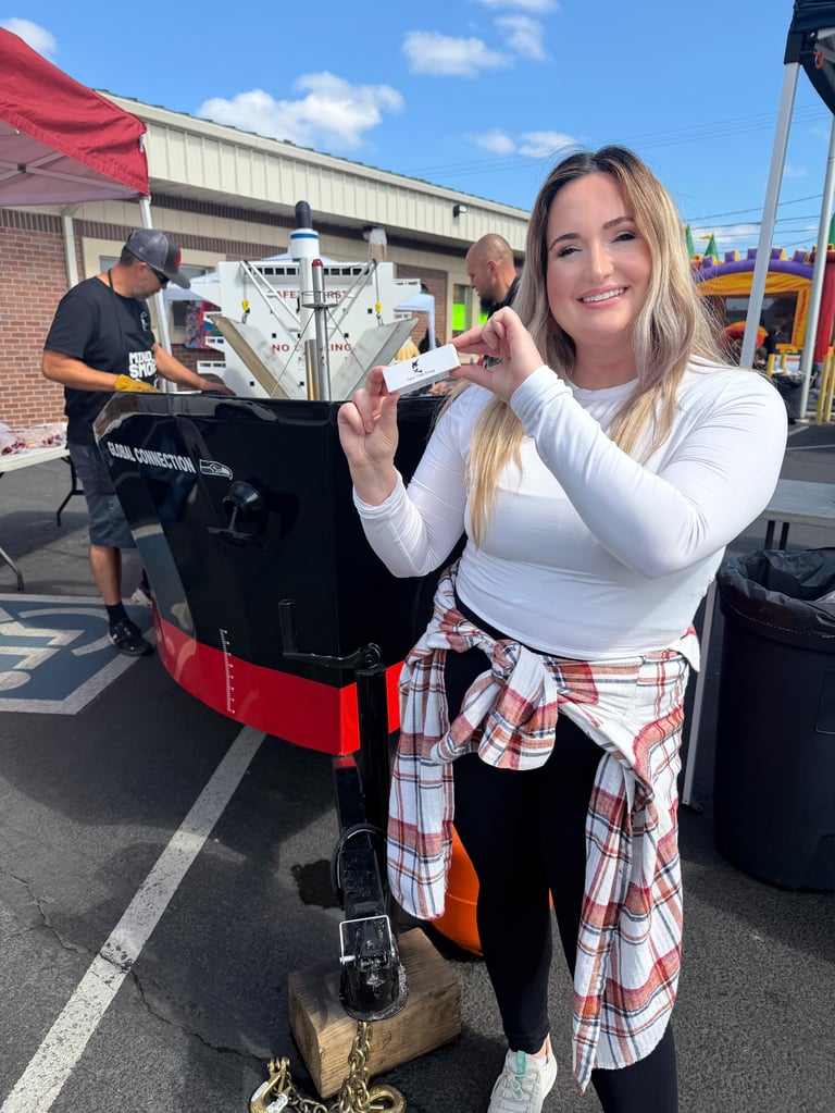 Woman smiling at camera holding a custom pickup truck bed at an outdoor event with vendors in background